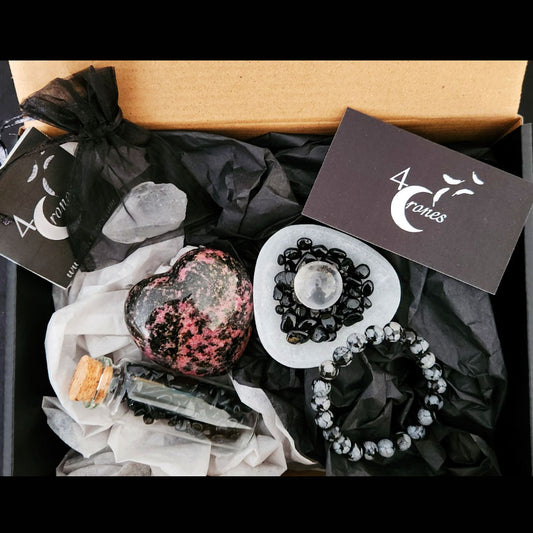 Snowflake obsidian bracelet, rhodonite heart-shaped stone, and jar with black tourmaline stone chips. Selenite triangular bowl with mini crystal quartz sphere.