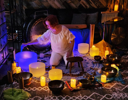 Woman in a room with singing bowls, candles, and other instruments creating a serene atmosphere. 4 crones