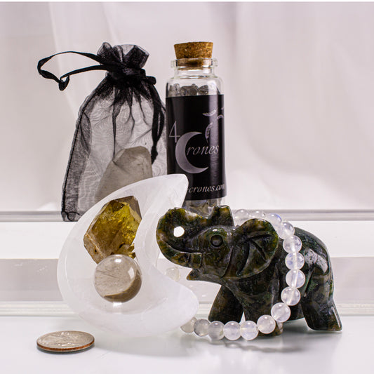 Decorative elephant figurine with beads, crystal ball, and bottle labeled '4 Crones' on a white surface.